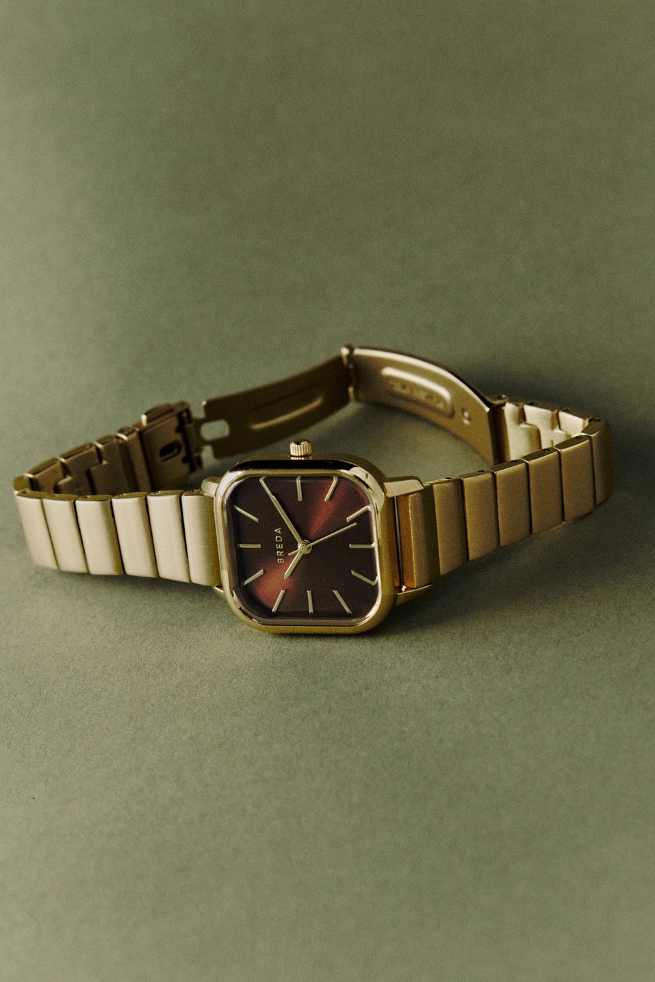 Gold watch with espresso color fill in square case on a sage green background 