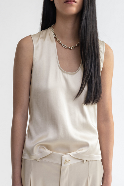 Woman wearing a beige sleeveless top and pants with a white background