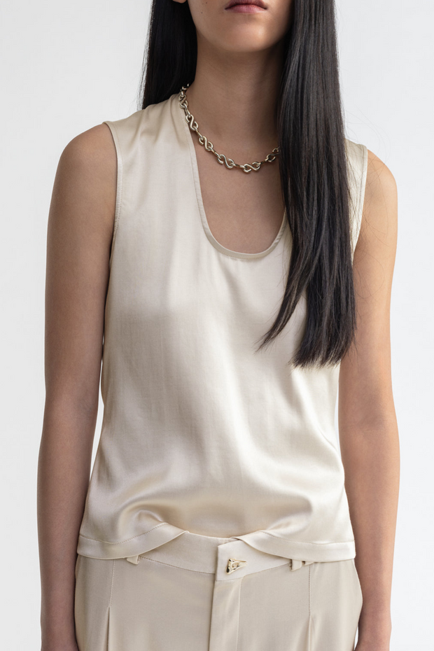 Woman wearing a beige sleeveless top and pants with a white background