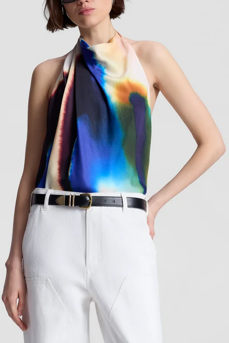 Woman wearing a colorful halter top and white pants on a plain background