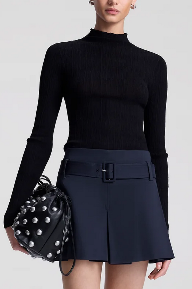 Person wearing a black long-sleeve top and navy shorts holding a black studded handbag on a light gray background