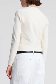 Person wearing a off white sweater and white pants with a black belt on a plain background