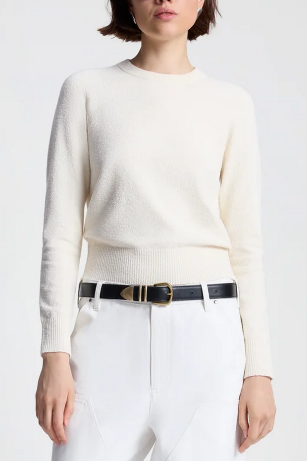 Person wearing a off white sweater and white pants with a black belt on a white background