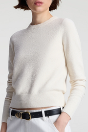 Person wearing a off white sweater with a black belt on a plain background