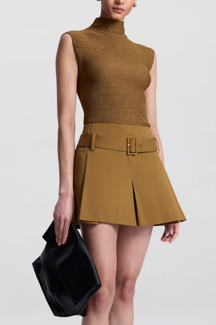 Woman wearing a mustard yellow sleeveless top and skirt with a black clutch against a white background