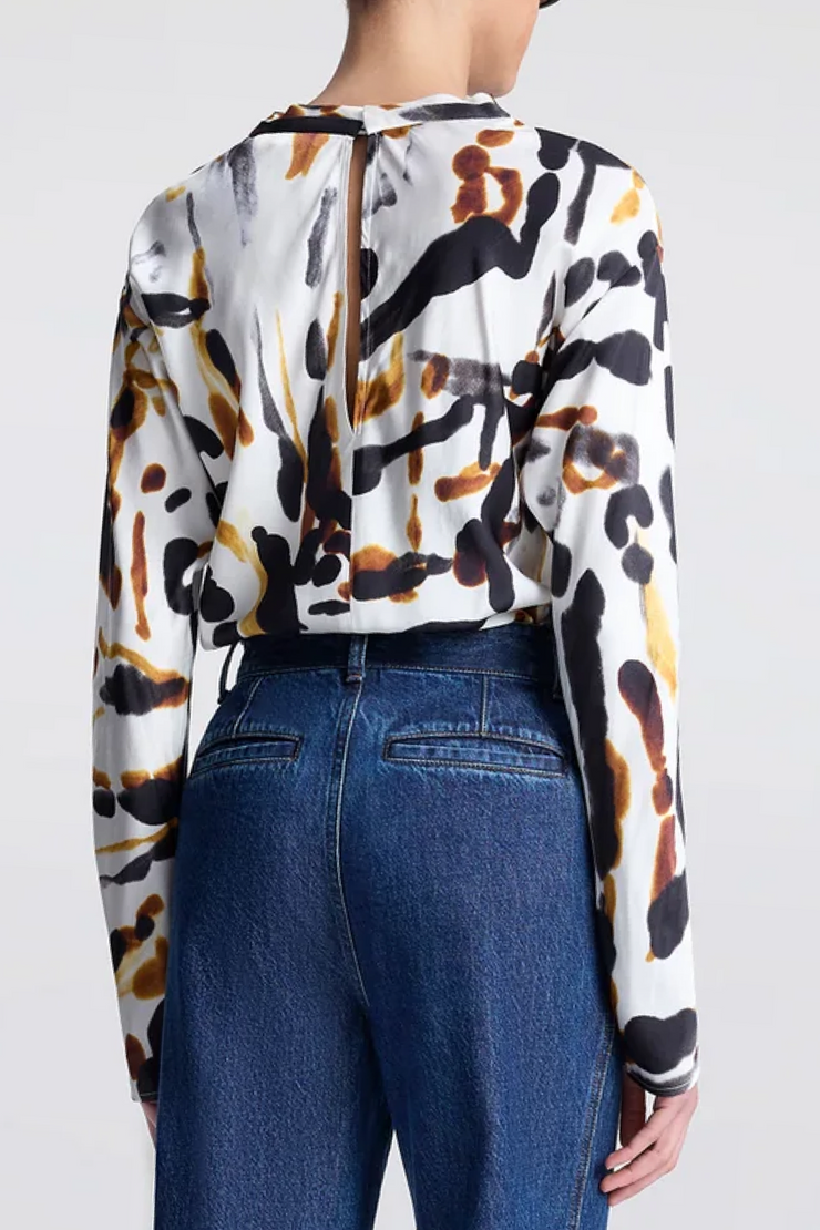 Person wearing a long-sleeve top with a colorful abstract pattern and blue jeans on a white background