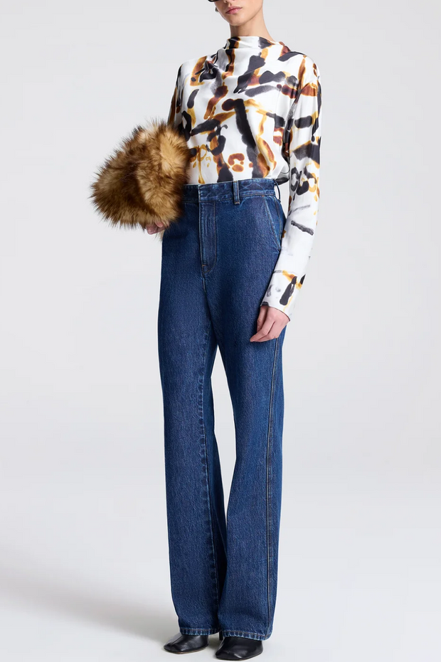 Person wearing a patterned blouse and blue jeans with a fur bag on a light gray background