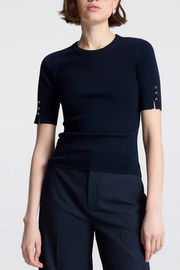 Person wearing a navy blue top with short sleeves and button details on a white background