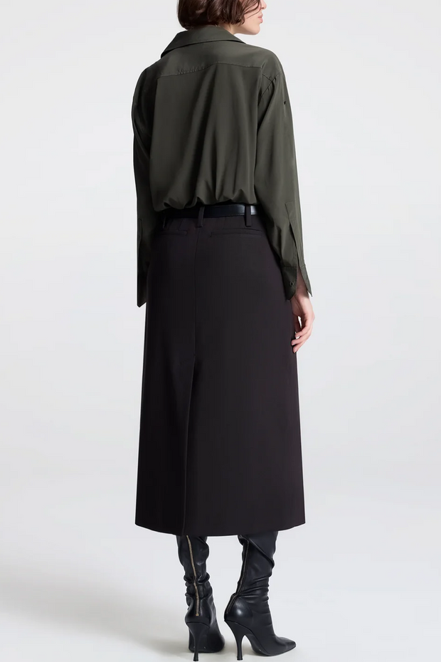 Person wearing a long green shirt and black skirt on a white background
