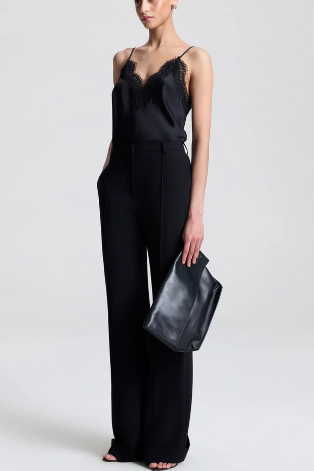 Person wearing a black jumpsuit holding a black clutch against a white background
