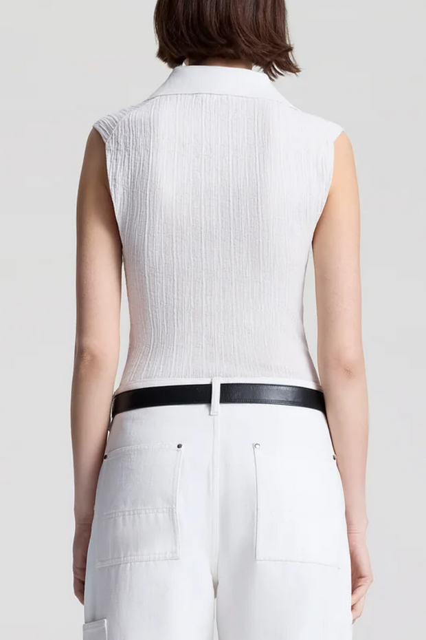 Person wearing a white sleeveless top with a black belt against a plain background