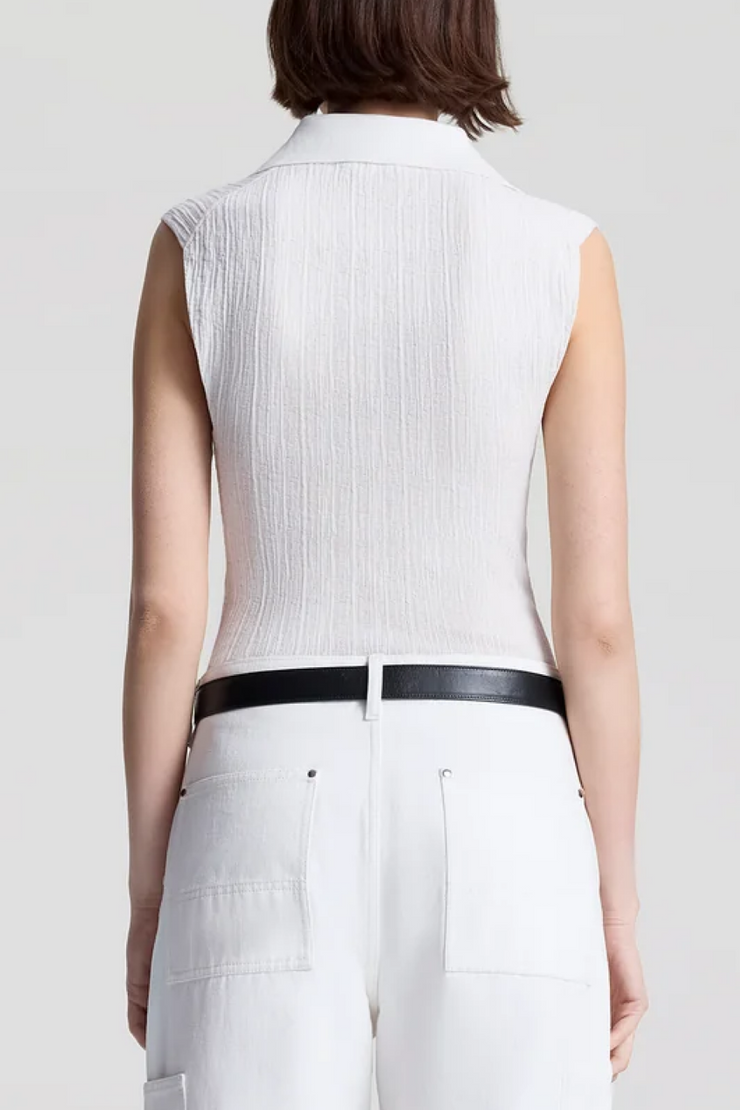 Person wearing a white sleeveless top with a black belt against a plain background