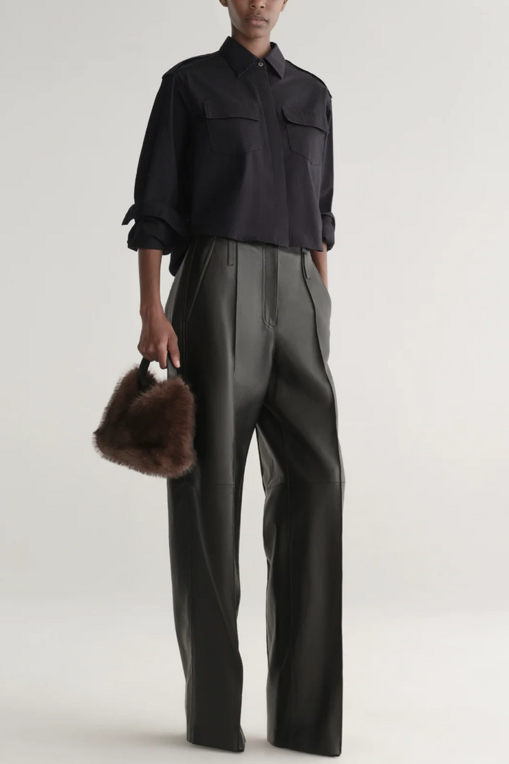 Person wearing a black shirt and gray pants holding a fur bag on a plain background