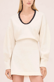 Woman wearing a cream-colored sweater dress with black trim on a light pink background