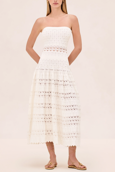 Woman wearing a white strapless dress with intricate detailing on a beige background