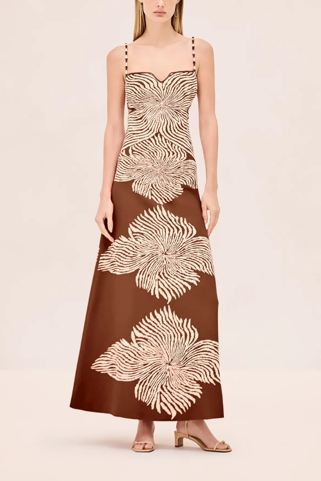 A woman modeling a sleeveless brown maxi dress with large cream floral and zebra-like abstract patterns, shown against a plain light beige studio background.