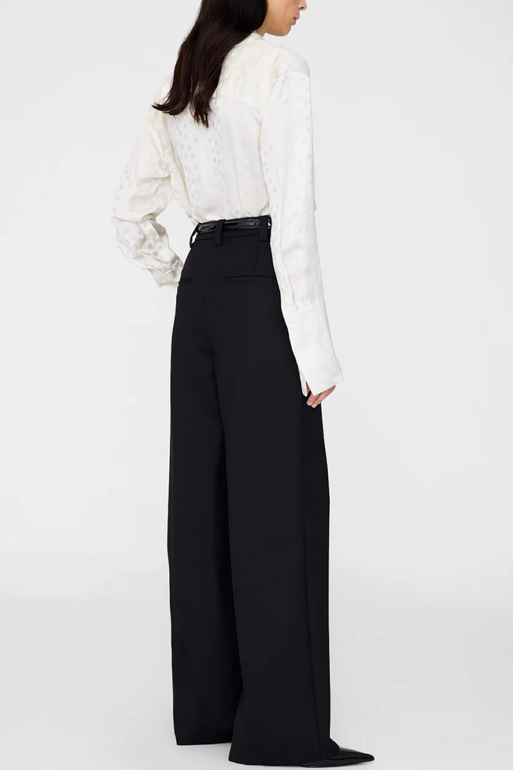 Person wearing a ivory dot blouse and black wide-leg pants on a white background