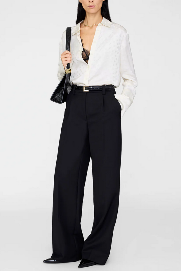 Person wearing an ivory dot blouse and black pants with a black handbag on a white background