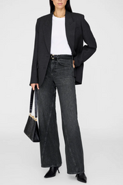 Person wearing a black blazer, white shirt, and dark jeans holding a black handbag on a white background