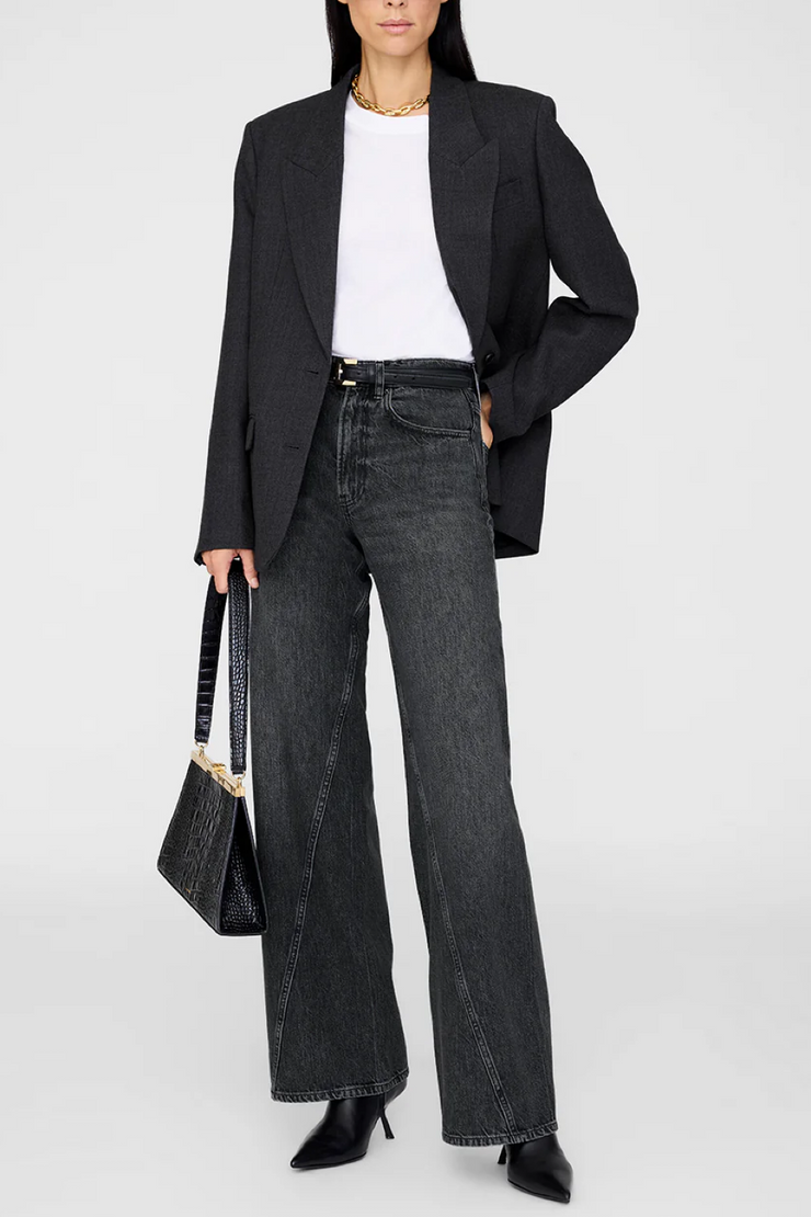 Person wearing a black blazer, white shirt, and dark jeans holding a black handbag on a white background