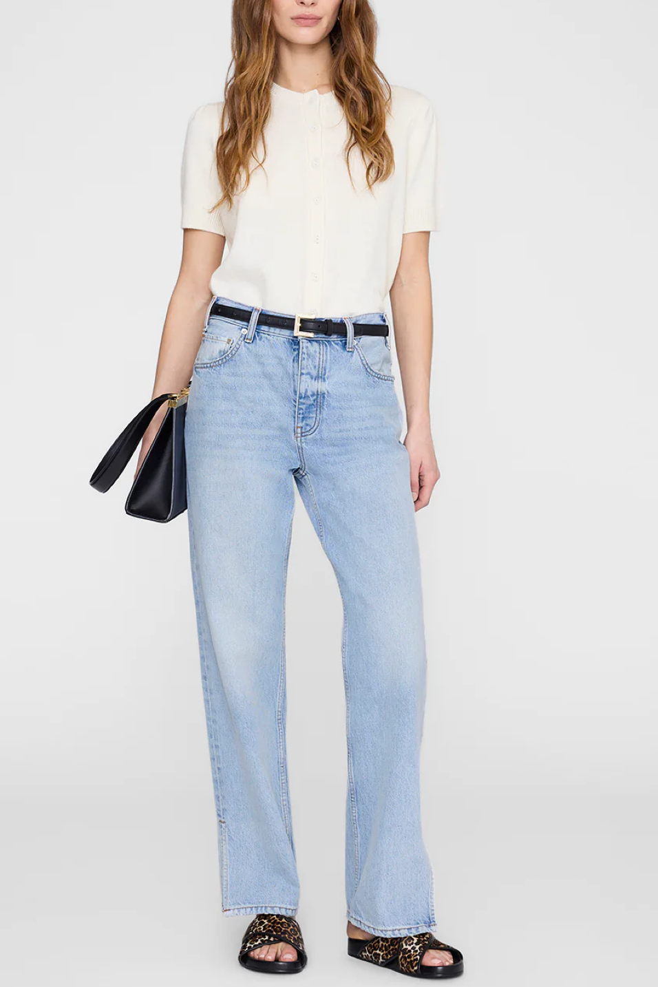 Woman wearing light blue jeans and a white top on a plain background