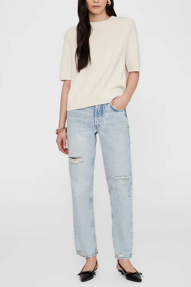 Person wearing a cream sweater and light blue jeans on a white background
