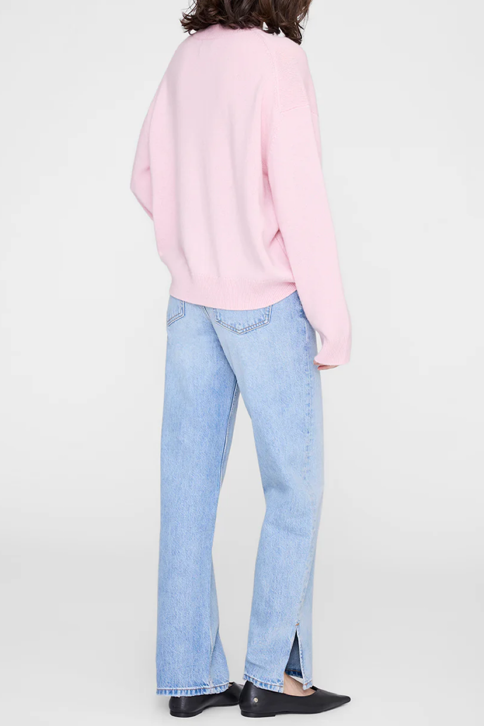 Person wearing a pink sweater and light blue jeans on a white background