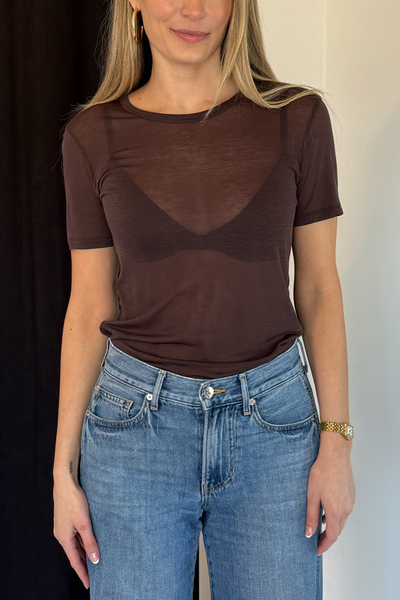Person wearing a sheer brown top and blue jeans against a neutral background