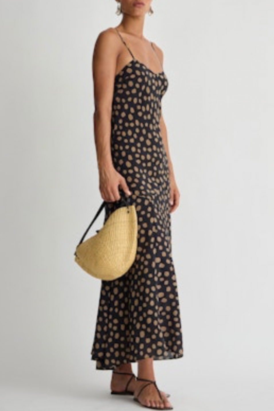Woman wearing a black dot dress holding a straw bag on a white background