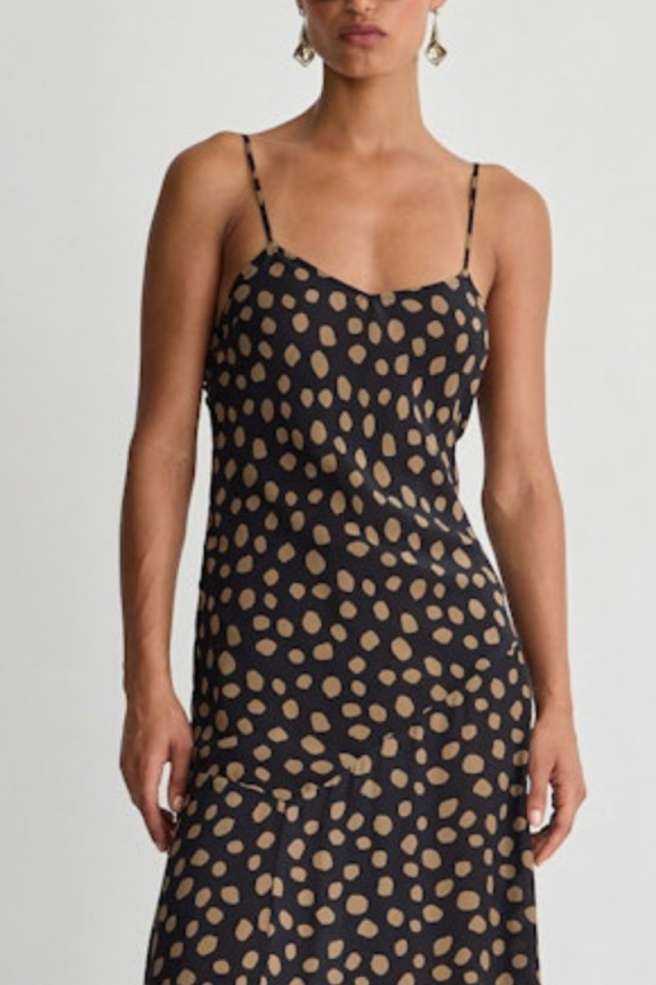 Woman wearing a black slip dress with beige dots pattern on a plain background