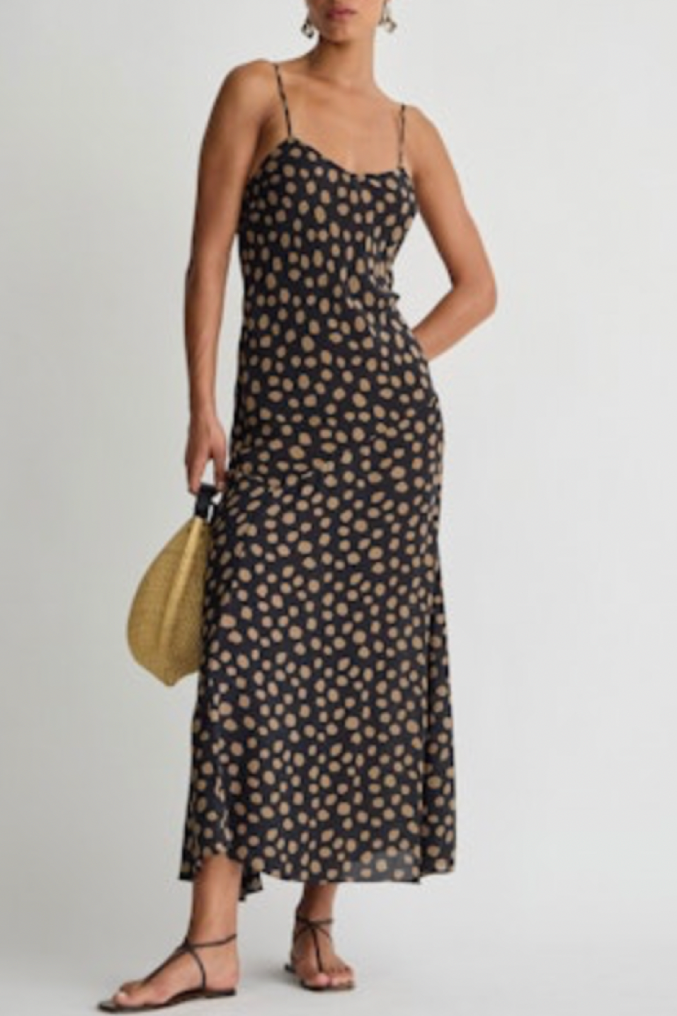 Woman wearing a black polka dot dress holding a yellow handbag on a light gray background