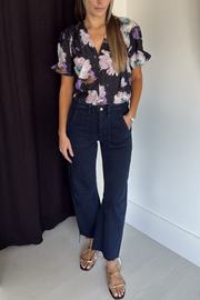 Woman wearing a floral blouse and dark jeans against a plain background