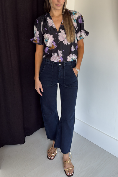 Woman wearing a floral blouse and dark jeans against a plain background
