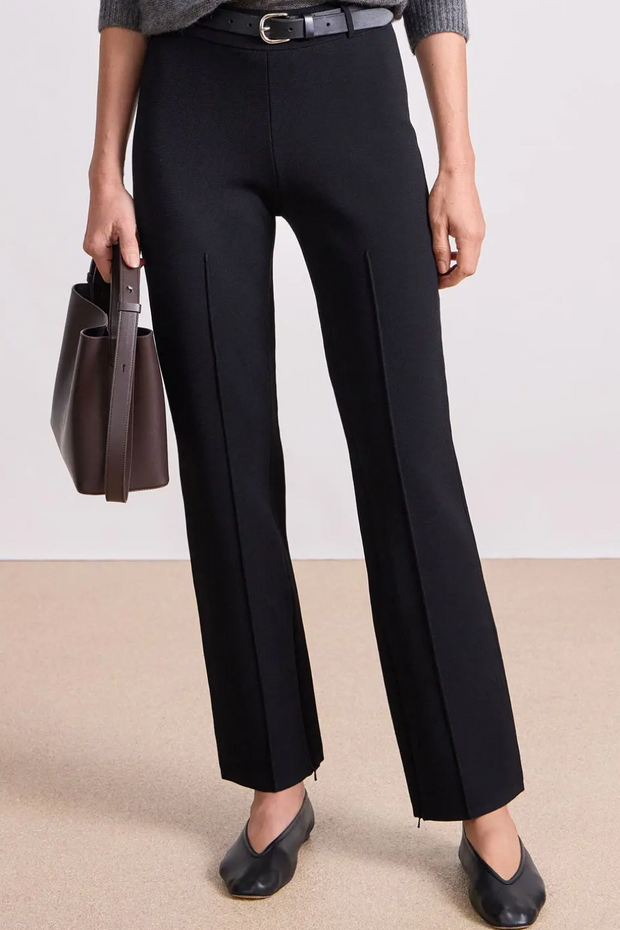 Person wearing black pants holding a brown handbag on a plain background