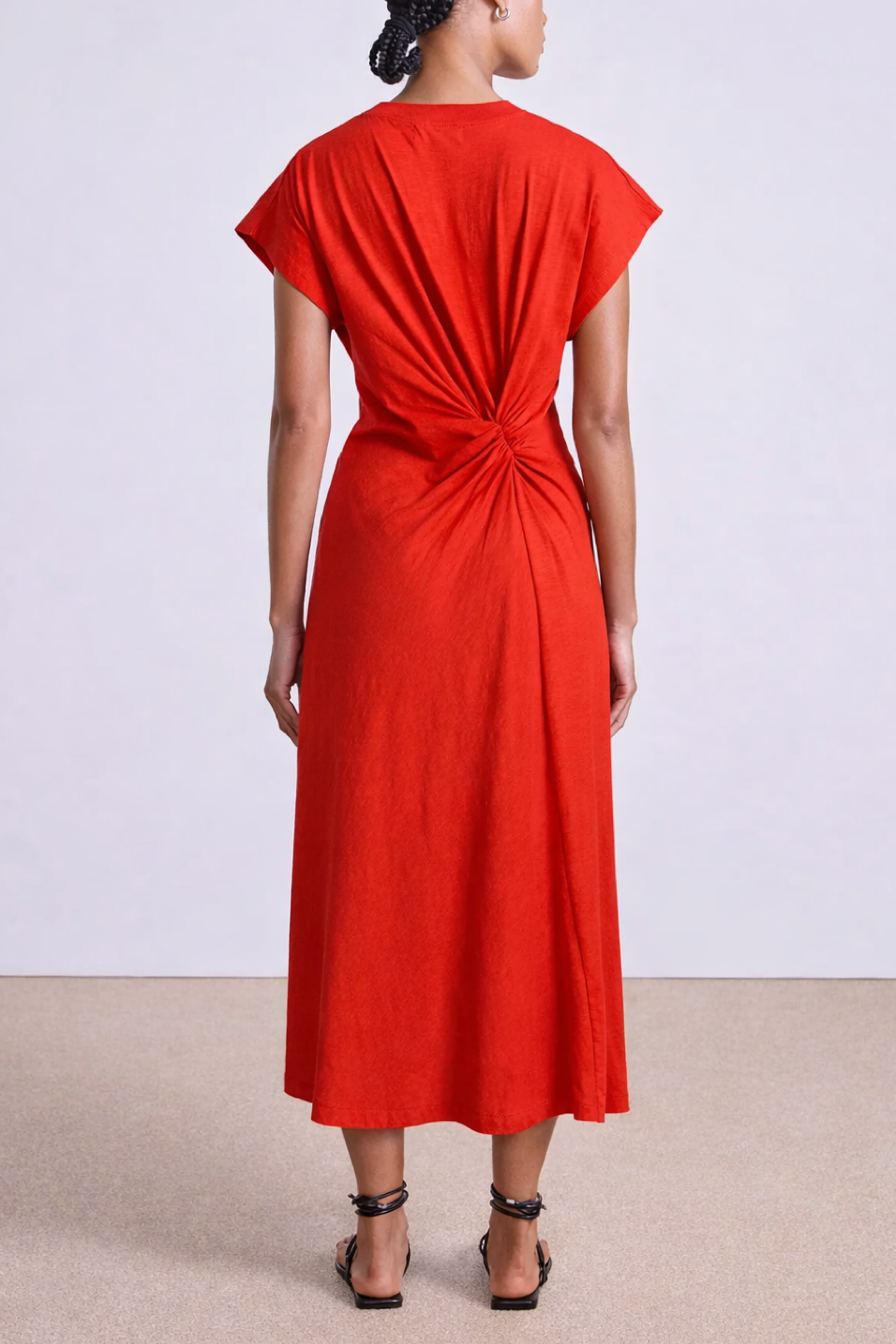 Person wearing a red dress with a knot detail on a plain background