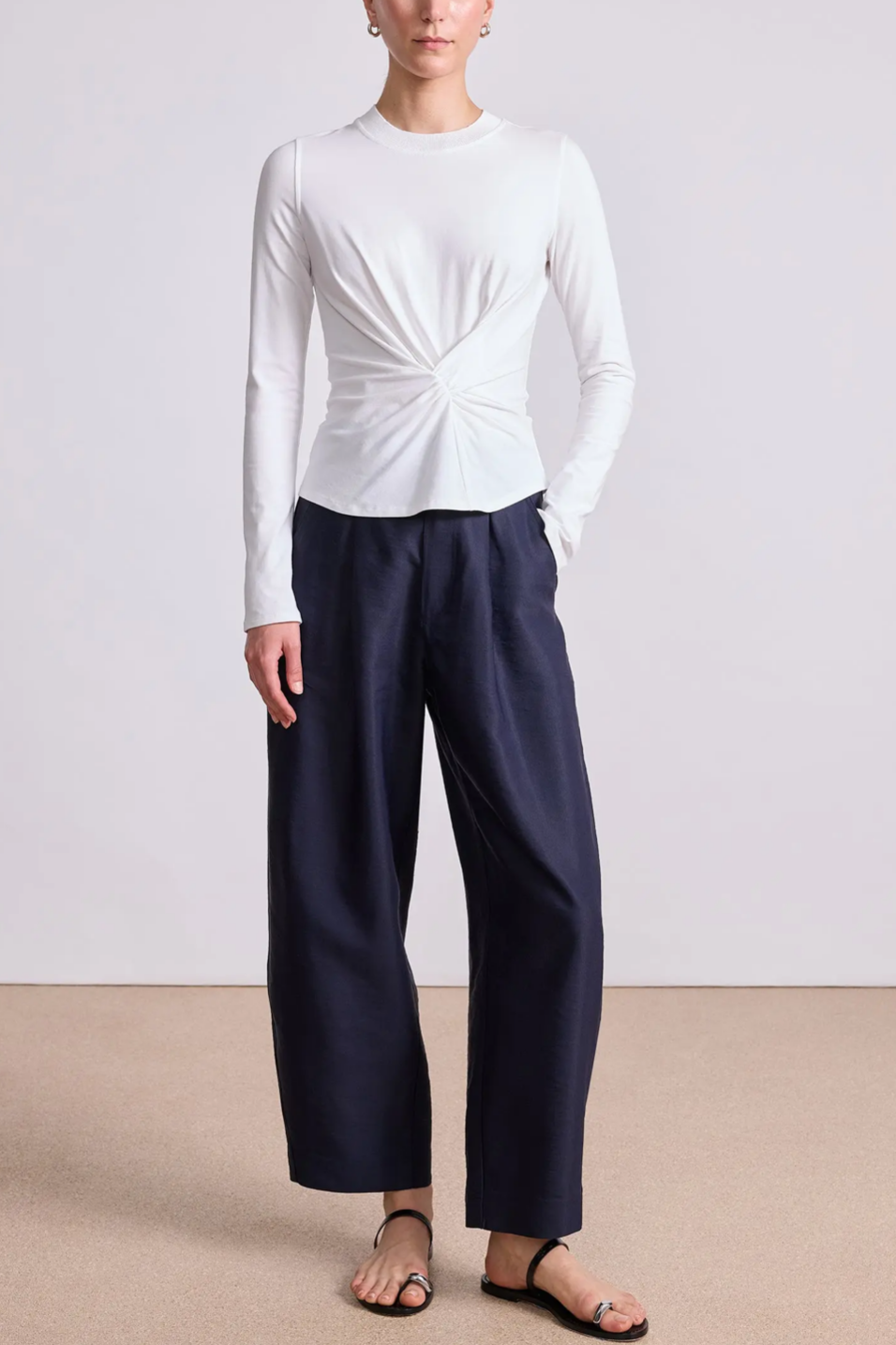 Person wearing a white long-sleeve top and navy pants on a plain background