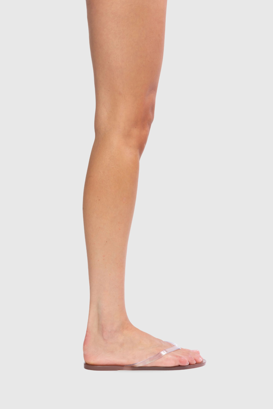 Clear sandal worn on a foot against a light gray background
