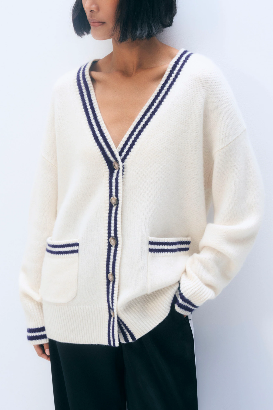 Person wearing a cream cardigan with navy trim on a white background