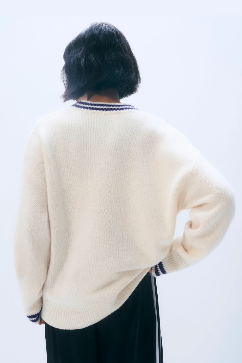 Person wearing a cream sweater with navy and white striped trim on a plain background