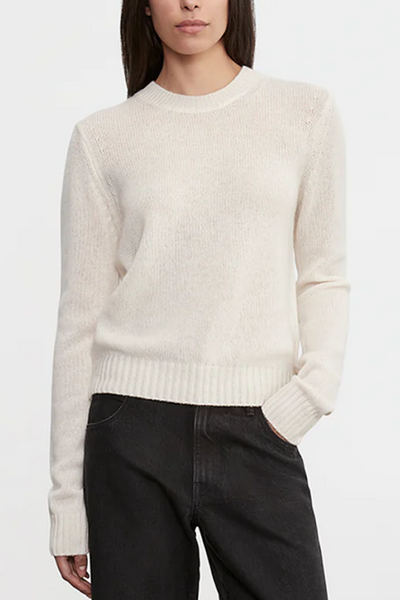 Person wearing a cream sweater and dark pants on a white background