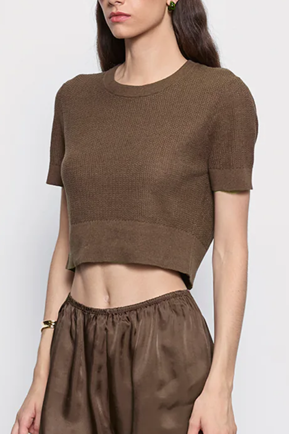 Woman wearing a brown cropped top and pants against a white background