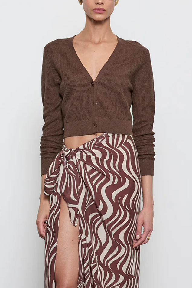 Person wearing a brown cardigan and patterned skirt on a white background