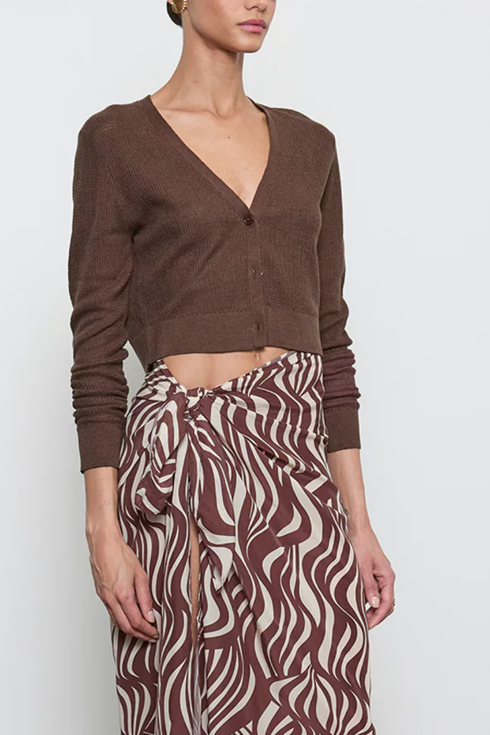 Woman wearing a brown cardigan and patterned skirt on a white background
