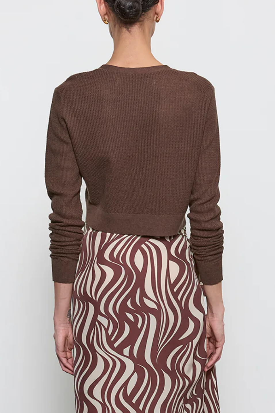 Person wearing a brown sweater and patterned skirt on a white background