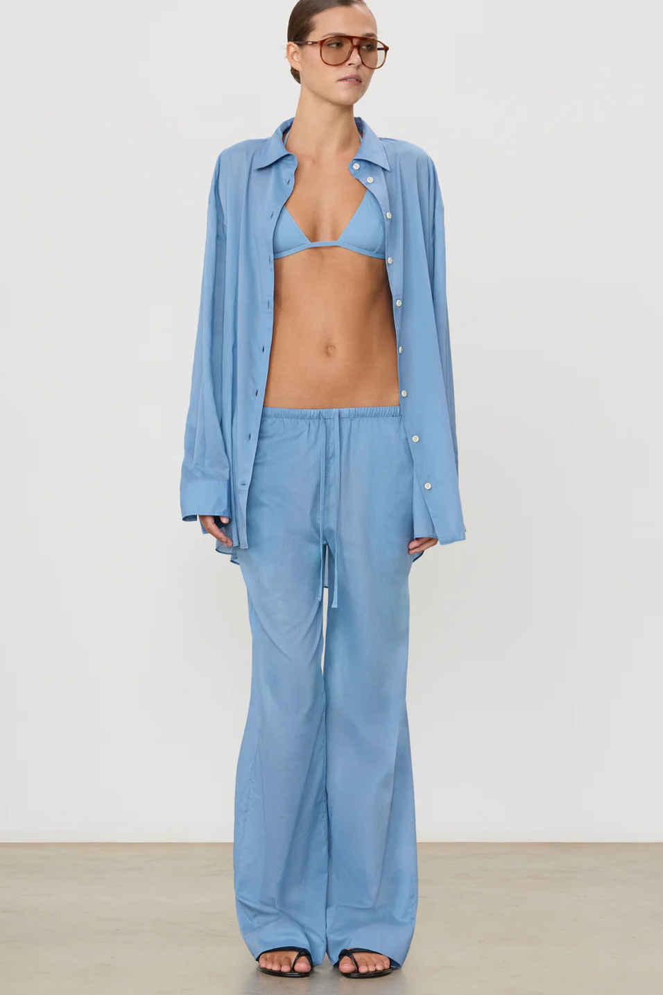 Woman wearing a light blue outfit with a shirt, bra, and pants on a plain background