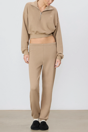 Person wearing a taupe sweatshirt and pants with a white background