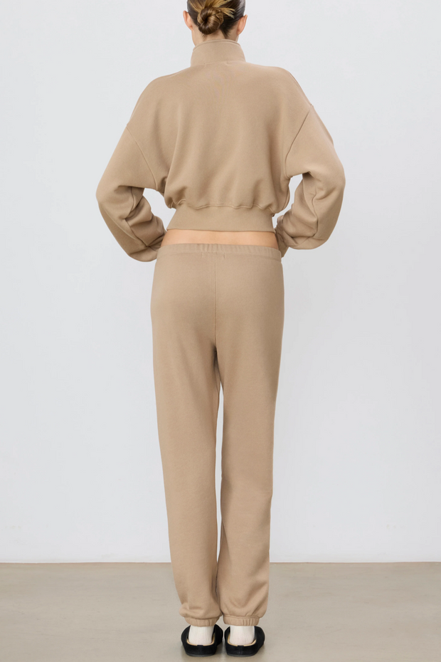 Person wearing a taupe sweatshirt and pants set on a white background
