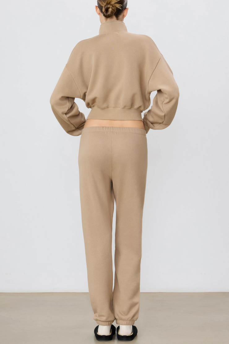 Person wearing a taupe sweatshirt and pants set on a white background
