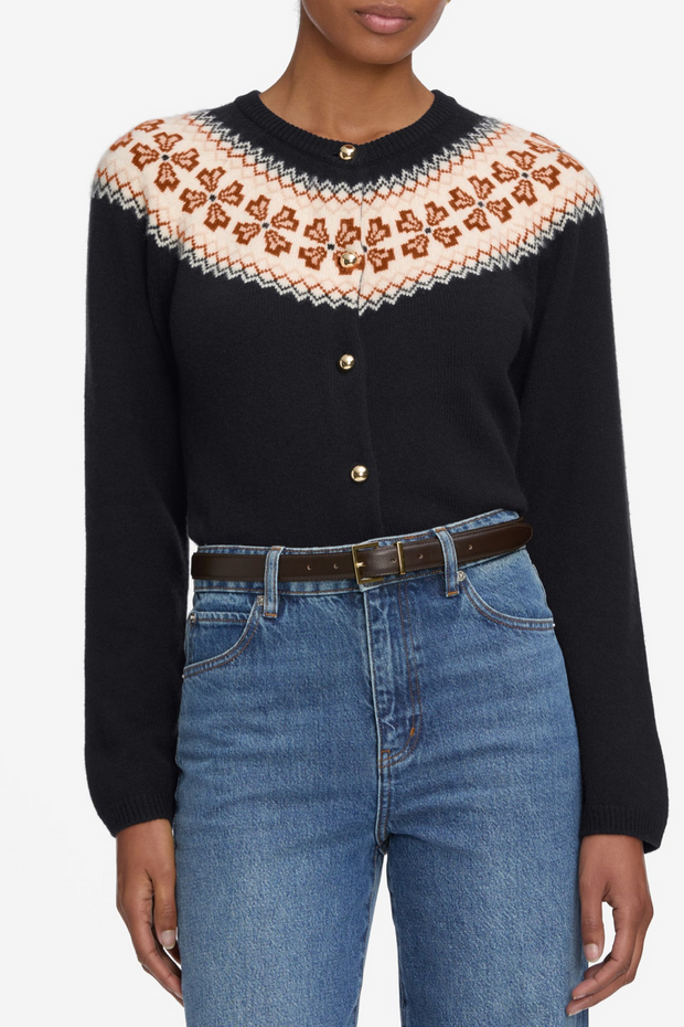 Person wearing a navy blue fairisle cardigan and blue jeans on a white background
