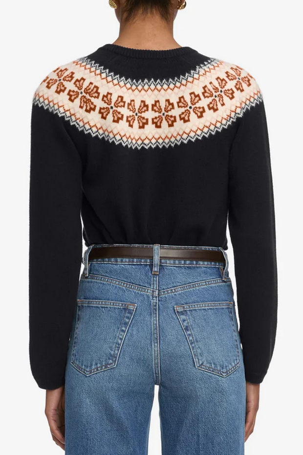Person wearing a navy blue fairisle cardigan and blue jeans on a white background